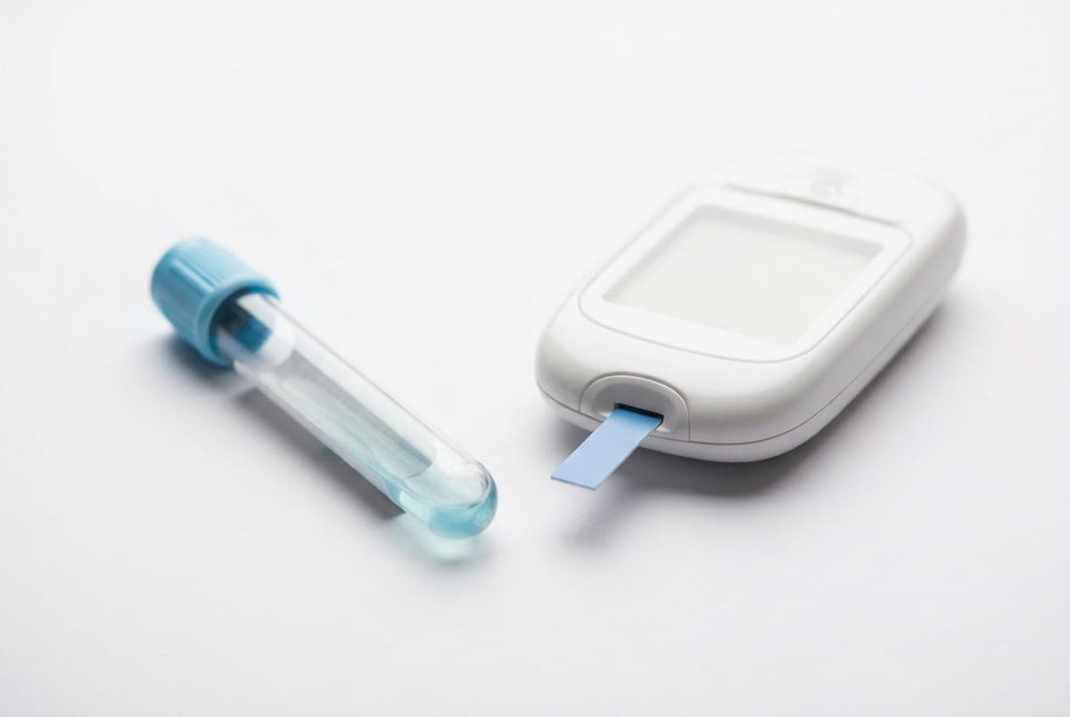 A laboratory blood sample tube beside a home glucose meter